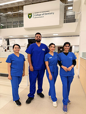 Four dental professionals in white lab coats standing together in a clinical laboratory.