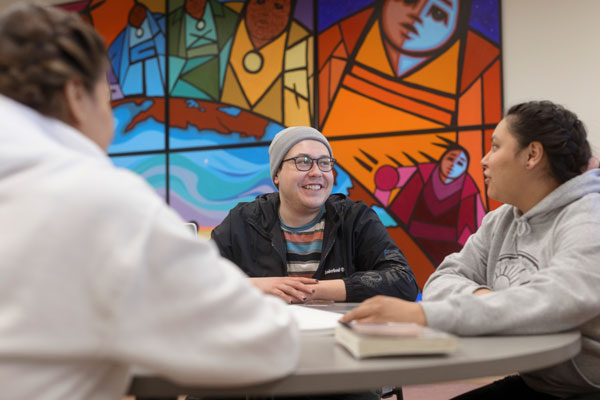 Two people sitting at a table with open books, in front of a colorful mural featuring abstract shapes and vibrant colors.