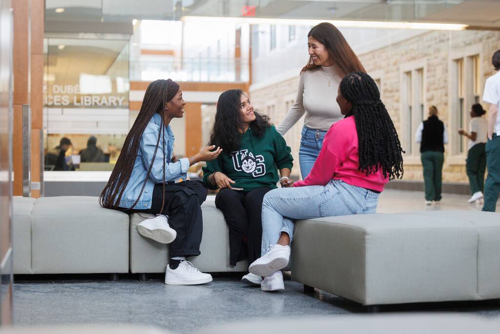 Five USask students chatting and laughing. It's fall. They walk down one of the pathways on the USask Saskatoon campus.