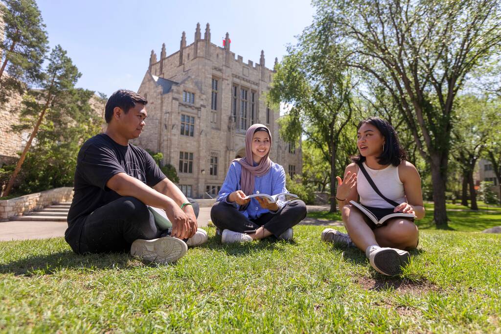 Three students sit on the lawn in front of the Thordvaldson building, Saskatoon campus.