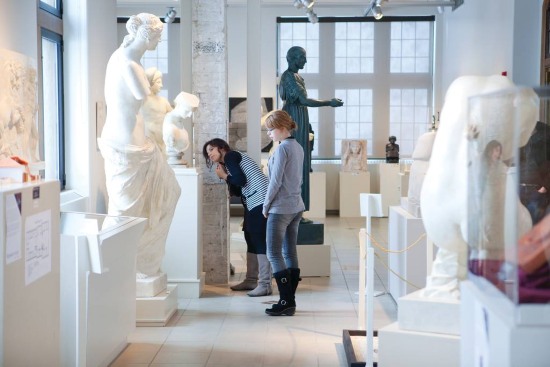 Students viewing classical sculptures inside a museum or gallery space.