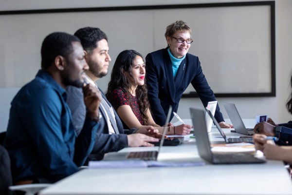 Group of students and a faculty member at a table with their laptops open.