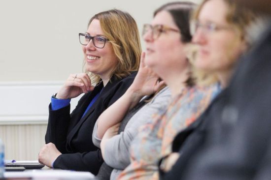 People seated side by side at a meeting table, listening during a discussion, with notebooks visible.