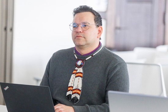 Person using a laptop at an office desk, wearing a beaded necktie.