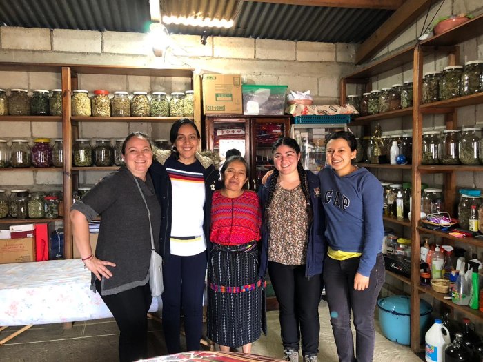 Five people standing together in a room with shelves of jars and supplies.