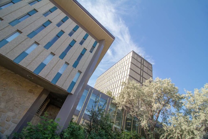 Exterior view of a modern university arts building with stone walls, tall windows, and trees