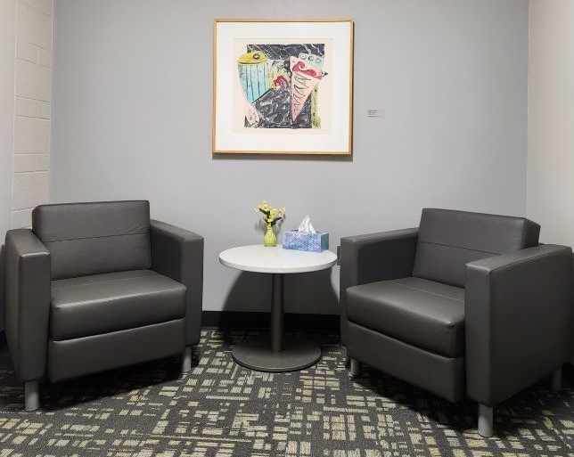 Two chairs with small table, tissues, and artwork in a clinic waiting room.